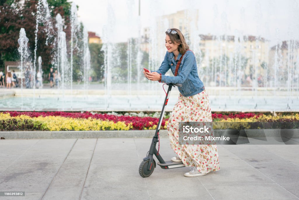 Woman with e-scooter in the city Young woman texting on her phone while leaning on her scooter Push Scooter Stock Photo