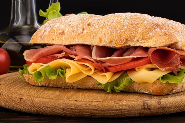 istock Ciabatta sandwich with lettuce , prosciutto and  cheese on wooden board 1180397813