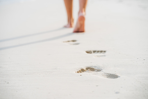 Caucasian young woman walking barefoot in sand, close up view.