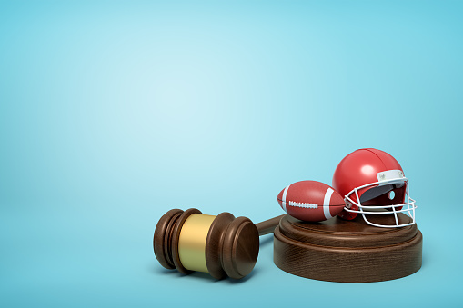 3d rendering of ball and helmet for American football on sounding block with judge gavel lying beside on light-blue background. Sport law cases. End up in court. American football seeks justice.