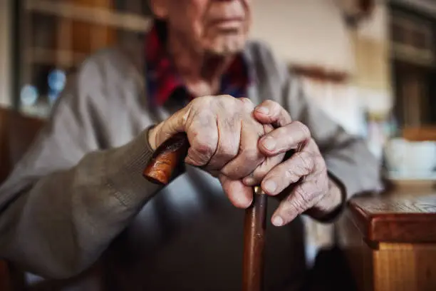 Cropped shot of an unrecognizable senior man leaning on his walking stick at home
