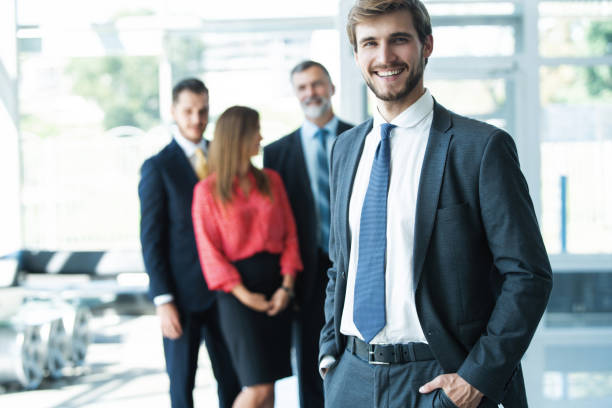 istock Team leader stands with coworkers in background 1180400663