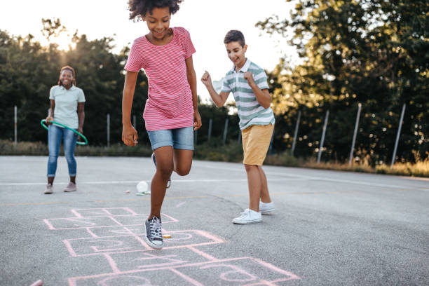 Doing what kids do best, jumping for joy Multi-ethnic group of kids playing hopscotch outside, jumping and  having fun schoolyard stock pictures, royalty-free photos & images