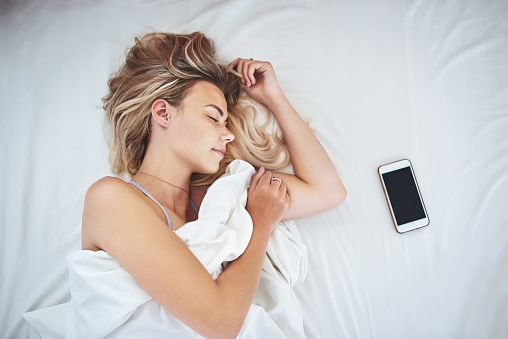 Cropped shot of an attractive young woman sleeping in her bed with her cellphone lying next to her