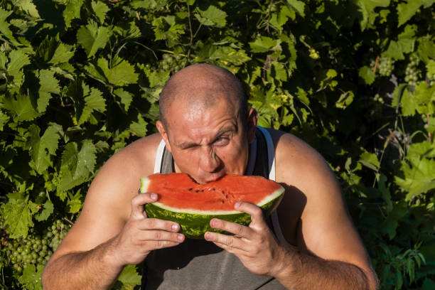 brutaler mann genießt süße rote wassermelone. 35-jährige männliche modell sitzt auf naturgrünen hintergrund und essen frisches obst. glücklich essen deich. - men 35 40 years male 30s stock-fotos und bilder