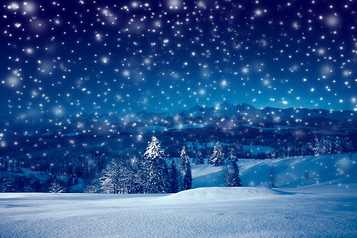 Beautiful Christmas night with snowfall. Christmas holiday landscape of mountains at starry night with blue sky