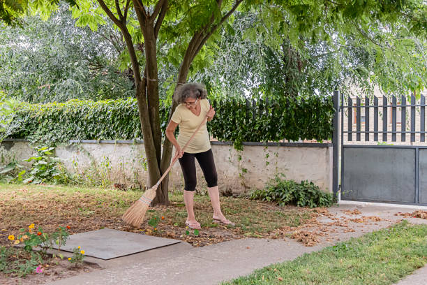 Senior Woman is Sweeping the Backyard with Broom