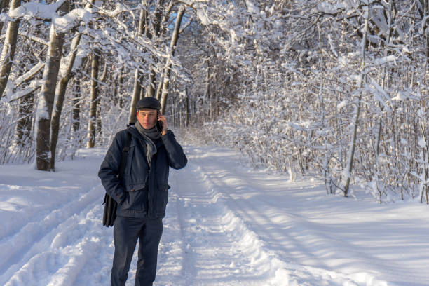 istock Handsome middle-aged man walking in winter snowy park or forest. Attractive man in jacket, scarf and cap talking on mobile phone. Winter mood, authentic lifestyle concept, stylish male outfit 1180411607