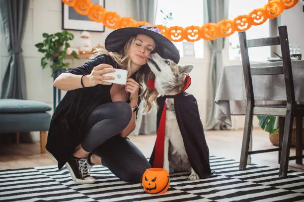 Woman and her pet dog wearing costumes at home for Halloween, woman making selfie for social networks