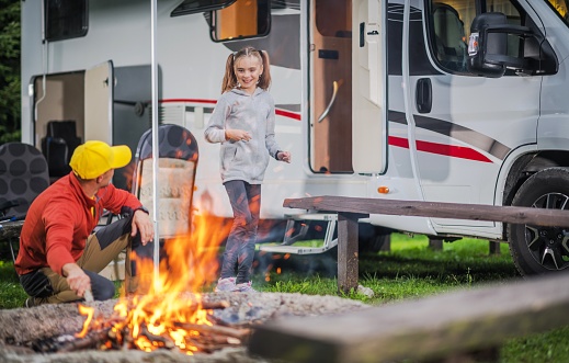 Family RV Road Trip Campsite. Caucasian Family. Father with Daughter Having Fun in Front of Campfire. Recreation Vehicle Traveling.