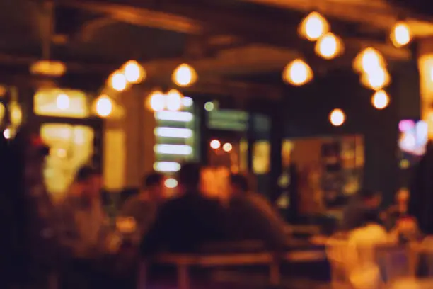 Blurred bokeh of the bar interiors with screens, retro lights and people sitting at tables toned in vintage style.