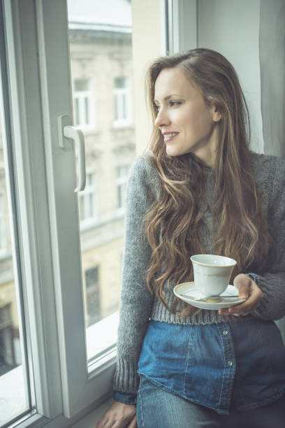 istock Beautiful woman drinking tea or coffee by the window 1180421641