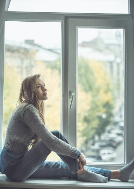 istock Beautiful young woman sitting by the window 1180421712