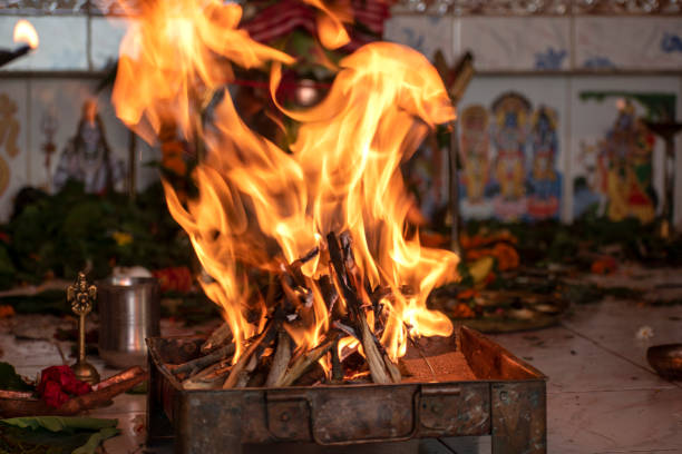 Panditji doing the Havan or yagna pooja. A pooja thali with some lamp, flower, coconut, copper pot, incense sticks, betel leaf, and camphor and the fire in the decorated clay or copper pot.