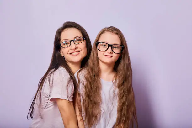 Happy young casual mother and smiling kid in fashion glasses hugging on purple background with empty copy space