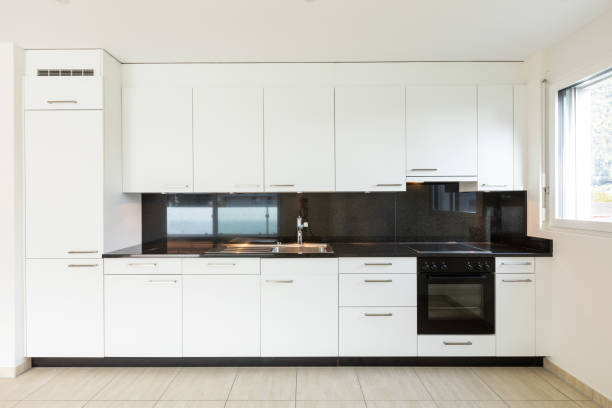 istock Empty room with white walls, travertine floor and white kitchen and black marble 1180432693