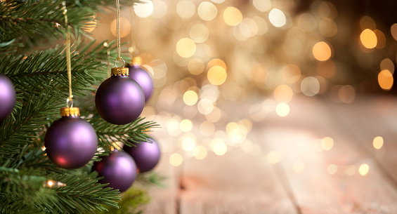 Christmas tree with purple baubles and gold lights against an old wood background