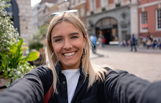 Young English woman taking a selfie outdoors in London and smiling towards the camera