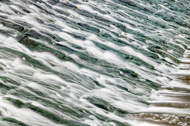 로프웰 위어, 플리머스, 데본에서 조류 덮인 바위 위로 흐르는 물의 긴 노출 - weir 뉴스 사진 이미지