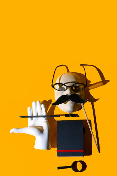 istock composition of various objects. Glasses, magnifying glass, pencil, mustache, butterfly, hand, notebook, mask. Form the image of a business person. Hard shadows on a yellow background 1180440374