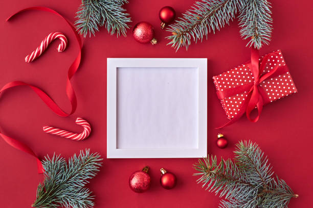 istock Mockup square white frame with red christmas balls, spruce branches and gift box on a red background 1180444740