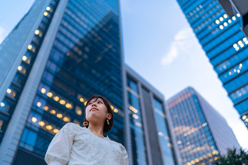 A portrait of young business woman in front of tall skyscrapers while looking away.