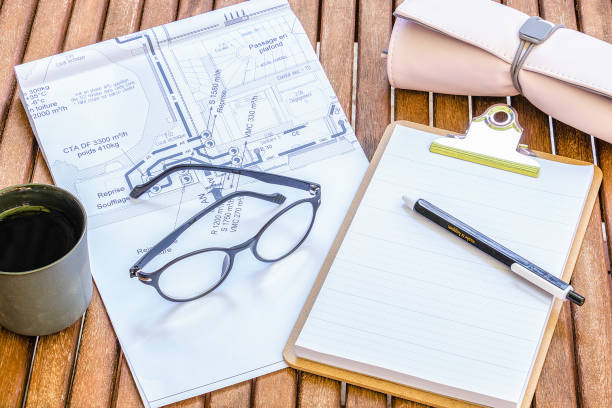 Architect's office or building engineer - female wooden office with a construction plan and office supplies glasses coffee cup pen kit stock photo