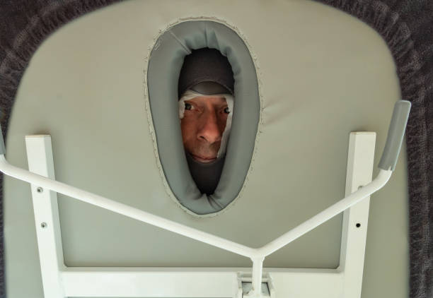 patient at the physiotherapist during a massage - man face seen from below the massage table through the hole of the head rest at the masseur in the hospital or rehabilitation center - massage table imagens e fotografias de stock