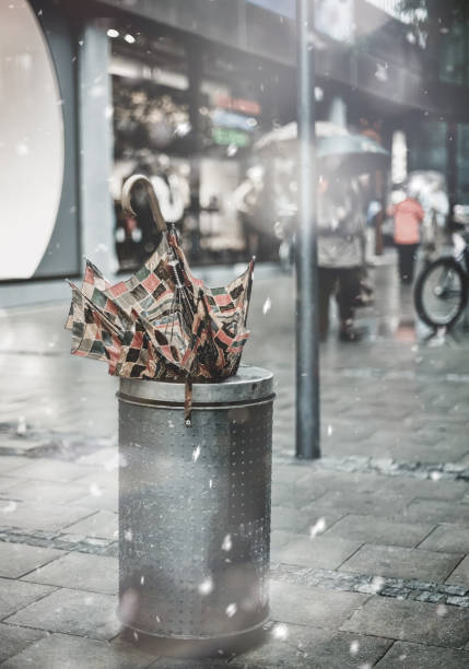 Broken umbrella in trash bin on shopping street district in winter snowstorm. Pastel trendy toning. Beautiful inspiring moody faded scenery