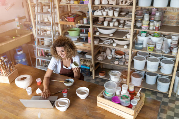 アートスタジオでラップトップを使用した女性陶芸家 - potter small business pottery happiness ストックフォトと画像