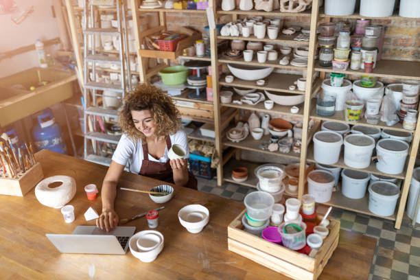 Female potter using laptop in art studio Female potter using laptop in art studio pottery making stock pictures, royalty-free photos & images
