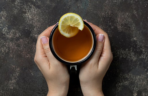 Herbal tea on dark background. Woman holding mug.