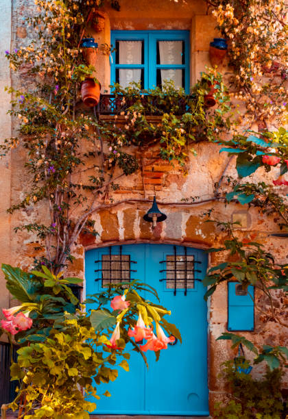 a beautiful house front with a blue door, blue window and flowers all over. - spain gerona architecture building exterior imagens e fotografias de stock