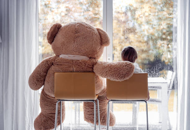 guardando la pioggia autunnale. ragazzino seduto con il suo grande morbido amico orsacchiotto sulle sedie ione anteriore della finestra guardando fuori. stile di vita autunnale. frendship. umore stagionale - teddy bear baby toy stuffed animal foto e immagini stock