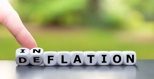 Hand turns a dice and changes the word "deflation" to "inflation", or vice versa.