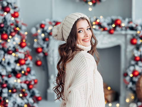 Adorable smiling girl with Santa red hat wearing white pullover holding a Christmas tree bouquet with new year decoration on white background. Christmas wish and dreams