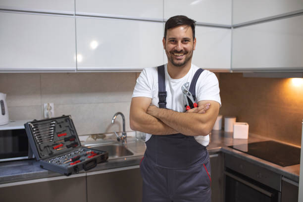 Young worker with tool bag standing near oven in kitchen. Smiling handsome plumber standing with crossed arms and looking at camera in kitchen. Portrait of a repairman on the kitchen. Service Industry: Mid-adult repairman working at customer's home. electrician smiling stock pictures, royalty-free photos & images