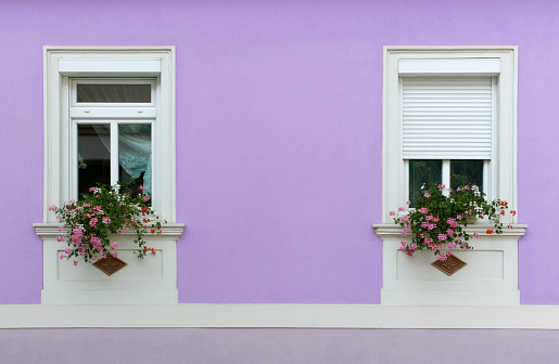 Close-up of the facade of an elegant house, with geranium flowerpots on the windowsills