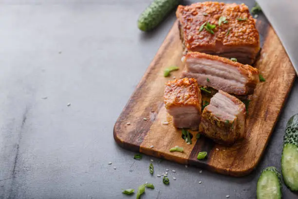 Photo of Chinese roasted pork belly on wooden cutting board copy space