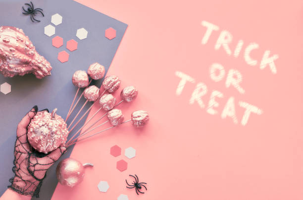 istock Creative Halloween flat lay on pink and grey split paper background with eyes and spiders. Hands in black mesh gloves holding decorations. Text 