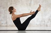 Sporty woman practicing yoga, doing Paripurna Navasana exercise