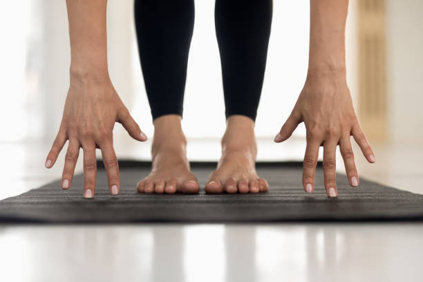 Woman practicing yoga, uttanasana pose, hands and feet close up Young woman wearing black sportswear, pants practicing yoga, standing in uttanasana pose, doin Head to knees exercise, hands and feet on mat close up, girl working out at home or in yoga studio knee to the head pose stock pictures, royalty-free photos & images