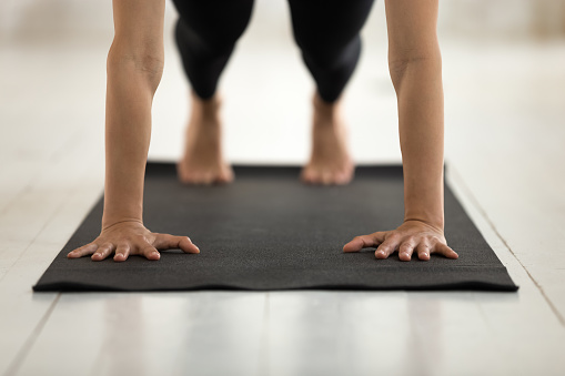 Young woman wearing black sportswear practicing yoga, doing Push ups or press ups exercise, standing in Plank pose, hands and feet on mat close up, girl working out at home or in yoga studio