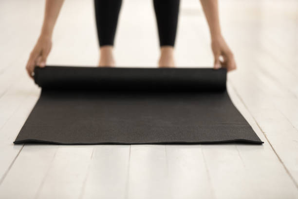 istock Woman practicing yoga, rolling black mat on floor close up 1180509548