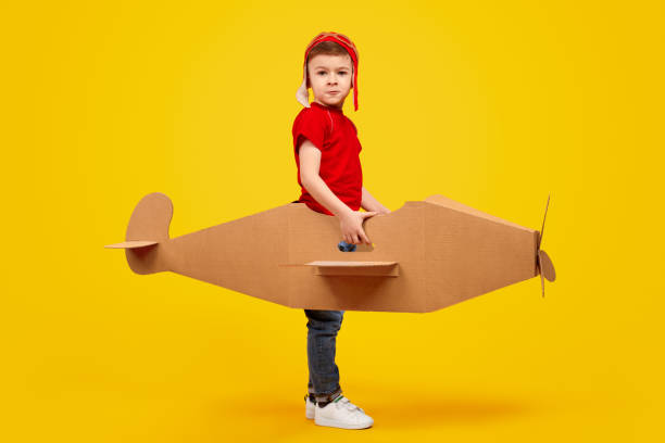istock Playful boy in helmet playing with handmade cardboard plane 1180509723