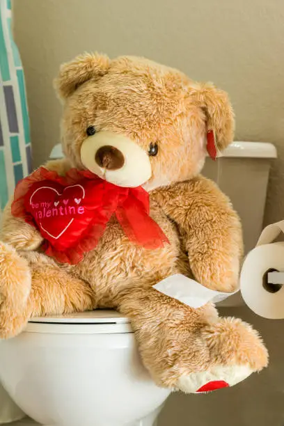 Photo of A teddy bear is in the restroom using the toilet. Portrait orientation.
