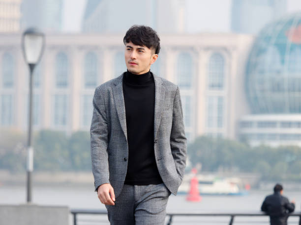 上海バンドの背景、中国のビジネスマンのライフスタイルの概念に対して彼のポケットに手で屋外を歩くカジュアルなスーツで自信とハンサムな中国の若いビジネスマン。 - asian ethnicity suit business men ストックフォトと画像