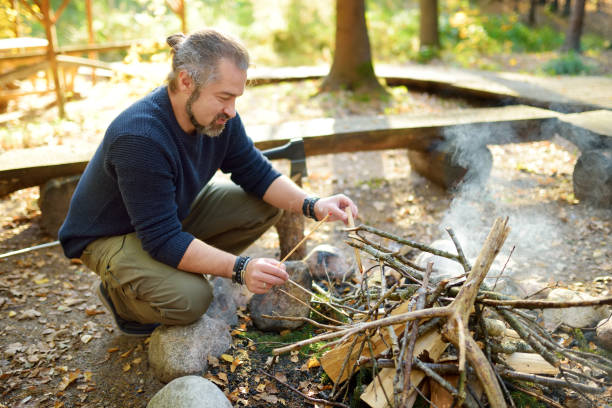 istock Young man starting a bonfire. Male tourist making a fire. Hiker having fun at camp fire. Camping in fall forest. 1180524150