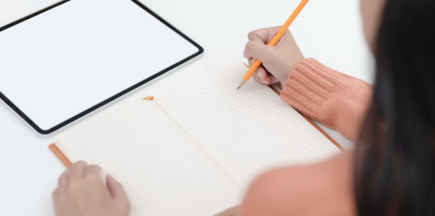 istock Close-up view of young female writing her idea on notebook while working on her project 1180529659