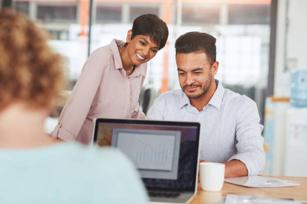 istock Two smiling coworkers using a laptop at an office desk 1180531601